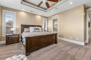 Bedroom with light carpet, a raised ceiling, a ceiling fan, recessed lighting, and ensuite bathroom
