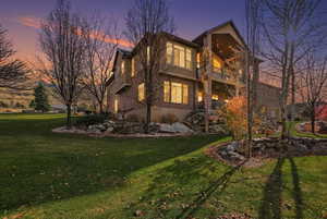 Back of house featuring stucco siding, a balcony, and a lawn