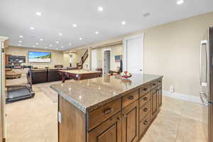 Kitchen featuring recessed lighting, a center island, pool table, light stone counters, and freestanding refrigerator