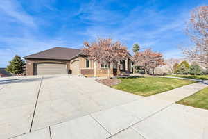 View of property hidden behind natural elements featuring a front yard, brick siding, driveway, an attached garage, and a shingled roof