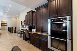 Kitchen featuring built in desk, double oven, dark brown cabinetry, recessed lighting, and light stone counters