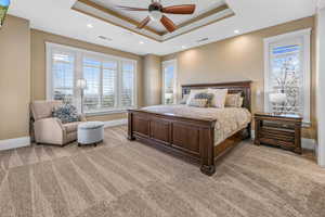 Bedroom with a tray ceiling, multiple windows, light carpet, a ceiling fan, and recessed lighting