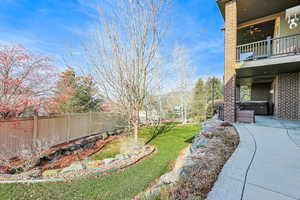 Fenced backyard with a hot tub, a patio area, ceiling fan, and a balcony