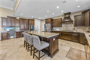 Kitchen featuring tasteful backsplash, a breakfast bar area, a kitchen island with sink, light stone counters, and dark brown cabinetry