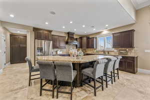 Kitchen with dark brown cabinets, a breakfast bar area, a center island with sink, backsplash, and stainless steel refrigerator with ice dispenser