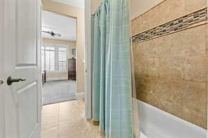 Bathroom featuring light tile patterned floors, ceiling fan, shower / bathtub combination with curtain, and light colored carpet