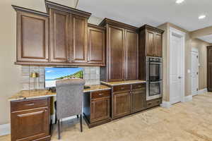 Kitchen featuring double oven, dark brown cabinets, light stone counters, decorative backsplash, and recessed lighting