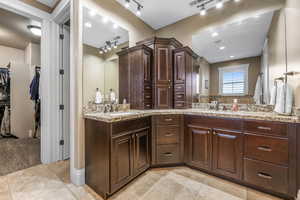 Full bath with double vanity, a spacious closet, rail lighting, and light tile patterned flooring