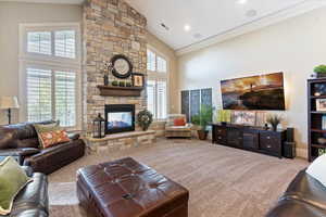 Carpeted living area with high vaulted ceiling, a stone fireplace, and ornamental molding