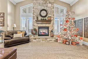 Living room featuring carpet floors, a stone fireplace, crown molding, and high vaulted ceiling