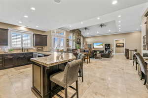 Kitchen with dark brown cabinets, a kitchen bar, a kitchen island, light stone countertops, and open floor plan