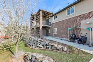 Back of house featuring stucco siding, a balcony, brick siding, and a lawn