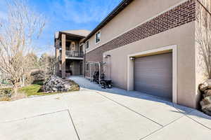 View of home's exterior featuring a balcony, stucco siding, a garage, driveway, and brick siding
