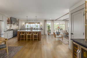 Kitchen with beverage cooler, pendant lighting, light wood-type flooring, wall chimney range hood, and recessed lighting