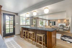 Kitchen with brown cabinets, light wood-style flooring, a breakfast bar, beamed ceiling, and open floor plan