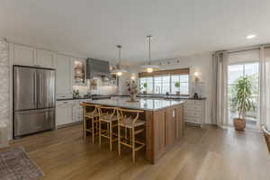 Kitchen with high quality fridge, decorative light fixtures, a kitchen island, dark stone countertops, and light wood finished floors