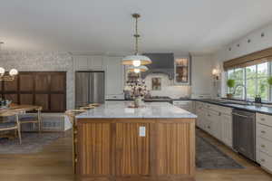 Kitchen featuring a kitchen island, dark stone counters, stainless steel appliances, glass insert cabinets, and hanging light fixtures