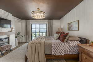 Bedroom with wood finished floors, a chandelier, a fireplace, and access to outside