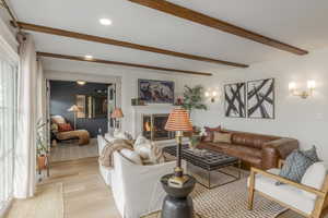 Living room with wood finished floors, beam ceiling, a warm lit fireplace, and recessed lighting