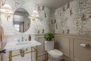 Half bath featuring wallpapered walls, wainscoting, a decorative wall, and vanity