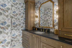 Bathroom featuring vanity, wallpapered walls, and ornamental molding