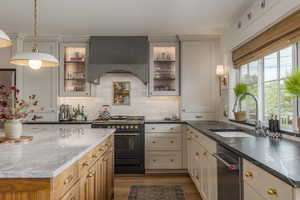 Kitchen featuring dark stone countertops, appliances with stainless steel finishes, wall chimney range hood, decorative light fixtures, and light wood-style flooring