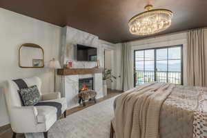 Bedroom with a high end fireplace, access to outside, wood finished floors, and a chandelier
