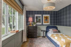 Bedroom with a decorative wall, a wainscoted wall, wallpapered walls, and light wood-type flooring