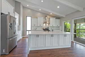 Kitchen with stainless steel appliances, light stone counters, tasteful backsplash, white cabinetry, and wall chimney range hood