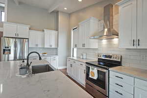 Kitchen featuring stainless steel appliances, wall chimney exhaust hood, white cabinets, light stone counters, and tasteful backsplash