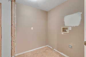 Washroom with a textured ceiling, hookup for a washing machine, and tile patterned flooring