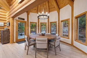 Dining space featuring a chandelier, light wood-type flooring, high vaulted ceiling, and a wooden ceiling with exposed beams