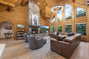 Living area featuring high vaulted ceiling, a fireplace, light wood-type flooring, log walls, and a wooden ceiling with exposed beams