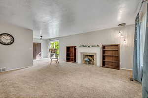 Unfurnished living room featuring a textured ceiling, light colored carpet, ceiling fan, and a fireplace with flush hearth