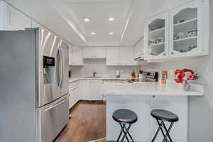 Kitchen with appliances with stainless steel finishes, glass insert cabinets, white cabinets, dark wood finished floors, and a peninsula