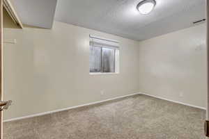 Carpeted empty room featuring a textured ceiling and baseboards
