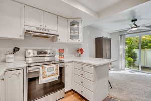 Kitchen featuring stainless steel range with electric cooktop, glass insert cabinets, under cabinet range hood, and white cabinetry