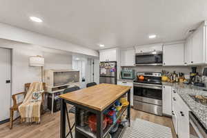Kitchen featuring a textured ceiling, stainless steel appliances, light wood-style floors, white cabinetry, and recessed lighting