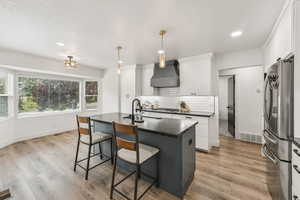 Kitchen featuring white cabinets, freestanding refrigerator, tasteful backsplash, a center island with sink, and a textured ceiling