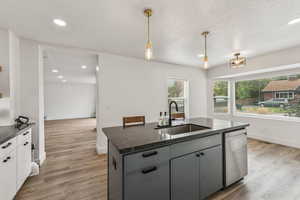Kitchen featuring gray cabinetry, hanging light fixtures, an island with sink, light wood-style floors, and recessed lighting