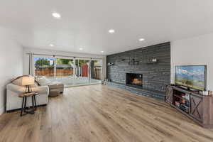 Living room featuring a stone fireplace, a textured ceiling, light wood-type flooring, and recessed lighting