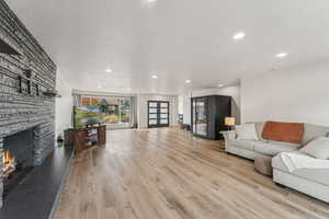 Living room featuring a stone fireplace, a textured ceiling, light wood-style flooring, and recessed lighting