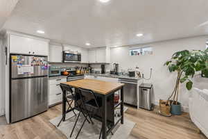 Kitchen with a textured ceiling, stainless steel appliances, light wood-style flooring, recessed lighting, and white cabinets