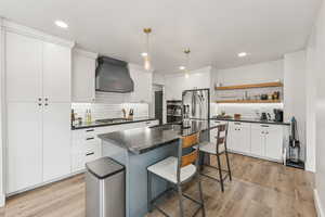 Kitchen featuring decorative backsplash, premium range hood, light wood-style floors, a kitchen breakfast bar, and hanging light fixtures