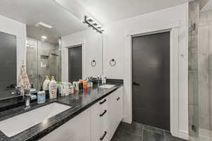 Bathroom featuring double vanity, a stall shower, a textured ceiling, and dark tile patterned floors