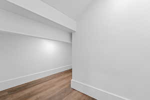 Hallway with wood finished floors and vaulted ceiling