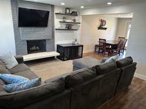 Living area with a brick fireplace, dark wood finished floors, and recessed lighting