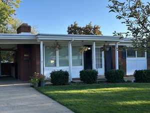 View of front of house with brick siding, a chimney, a front lawn, covered porch, and a carport