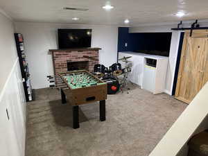 Playroom featuring a textured ceiling, a barn door, light carpet, a brick fireplace, and wooden walls