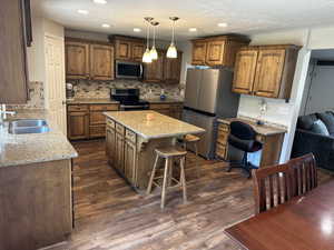 Kitchen with appliances with stainless steel finishes, a kitchen island, light stone countertops, dark wood-type flooring, and recessed lighting